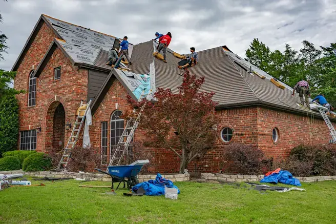 Roofing crew removing old shingles and installing underlayment on a brick house